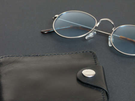glasses in gray frames with blue lenses next to a black leather wallet on a black backgroundの写真素材