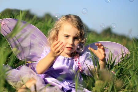 Girl fairy in the meadow catching soap bubbles