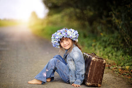 Joyful girl sitting on the street based on a suitcaseの写真素材