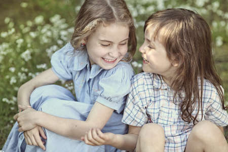 Two young girls sitting on green grass in the meadowの写真素材