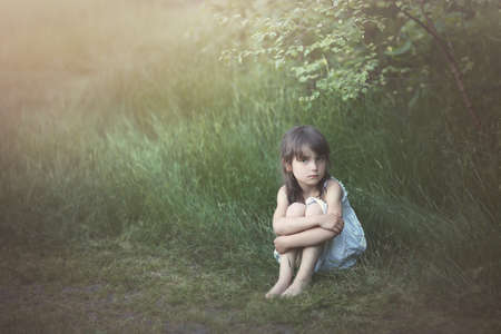 Pensive beautiful young girl on a green gladeの写真素材