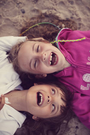 Two friends laughing while lying on the beachの写真素材