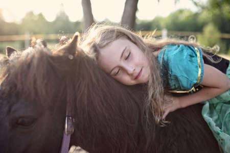 young girl in a dress hugging a ponyの写真素材