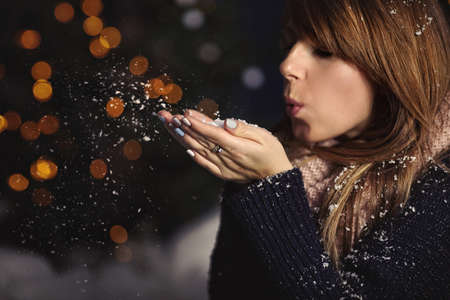 Girl blowing snowflakes in winter eveningの写真素材