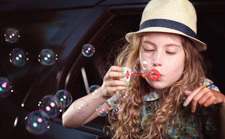 Blonde hair young girl lets soap bubbles in carの写真素材