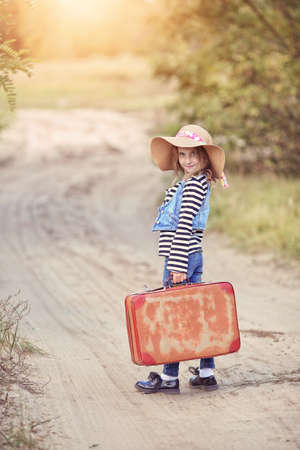 Smiling young girl in a hat and suitcaseの写真素材