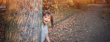 young girl hides behind a tree on a sunny dayの写真素材