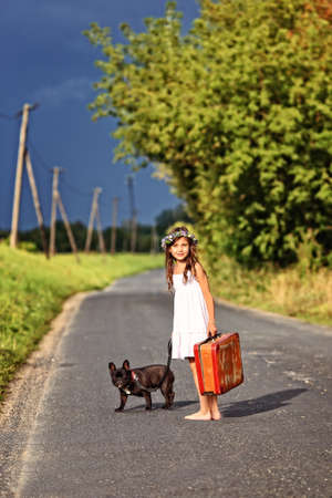 Happy young girl walks with a suitcase and a bulldogの写真素材