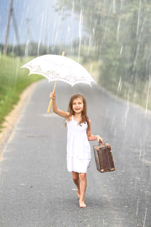 Young girl walks with suitcase and umbrella in the rainの写真素材