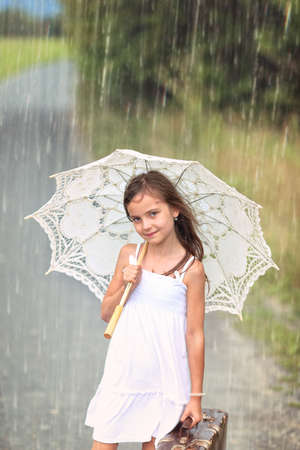 summer adventure trip - girl with suitcase and umbrella on a rainy summer dayの写真素材