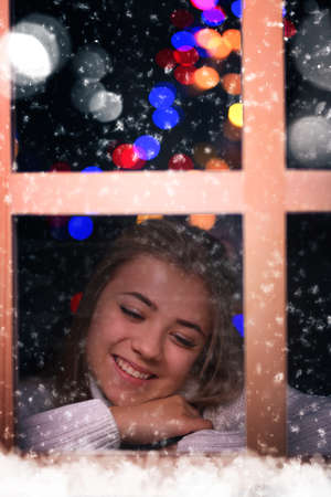 happy young girl looks out the window in winter Christmas eveningの写真素材