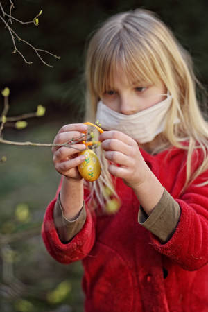 young girl in a mask hangs an Easter egg on the tree