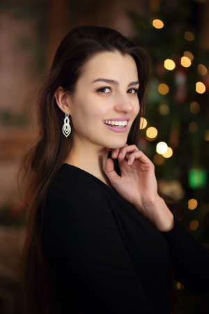 A young girl in a festive mood in a black dress by the Christmas treeの写真素材