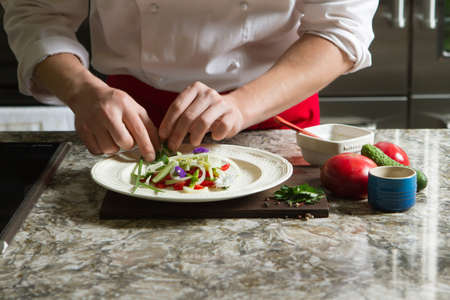 Chief cook in an pinafore preparing a salad in the kitchenの写真素材