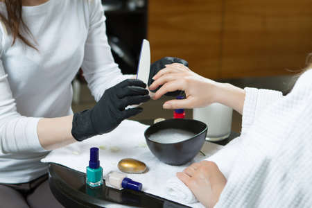 Closeup Of Woman Hands Receiving Manicure And Nail Care Procedure. Close-up Manicurist Polishing nails On Female Nails With Wooden Stick For Cuticle In Beauty Salon. 