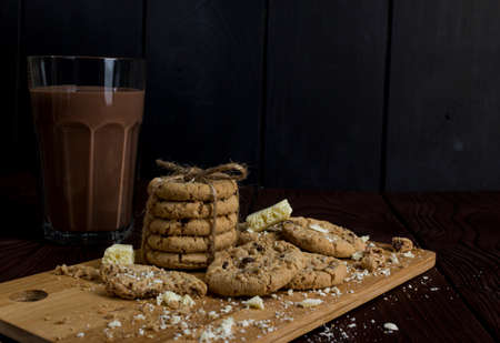 Light chocolate cookies with pieces of white porous chocolate and cocoa on a dark wooden table