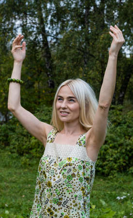 The smiling blonde held up her hands in the Park in a floral-patterned dress. Vertical photoの写真素材