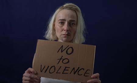 Bruises on the womans face. A woman holds a placard with the text NO TO VIOLENCE.の写真素材