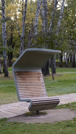 Beautiful wooden bench with metal visor in the park. Landscape design. Improvement of parks. Modern benches in the city square. City improvement, urban planning, public spaces.の写真素材