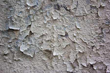 Old Weathered Painted White Plastered Peeled Wall Background. Cracked Flaked Shabby Wall With Rundown Stucco Layer Texture. Cracked peeled white paint with blue spots on an old stone wall.の写真素材