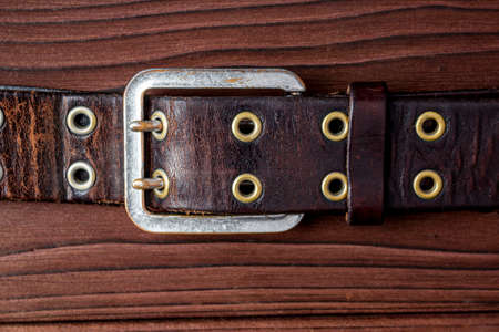 Old leather belt with a buckle on old wooden board. Mens brown belt made of genuine leather with a...