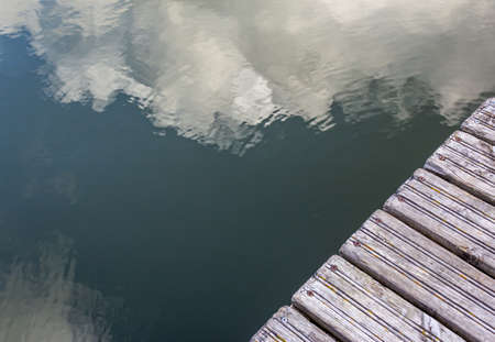 Pier in the river with reflections in the water, top view. Clouds are reflected in the water. Background with copy space. Two textures for the design. Pier made of old wooden planksの写真素材