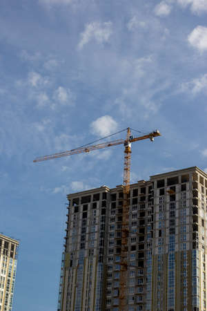 Construction crane is working on the construction of a multi-storey building, the view from the bottom of the crane on the construction crane and the building under construction against the skyの写真素材
