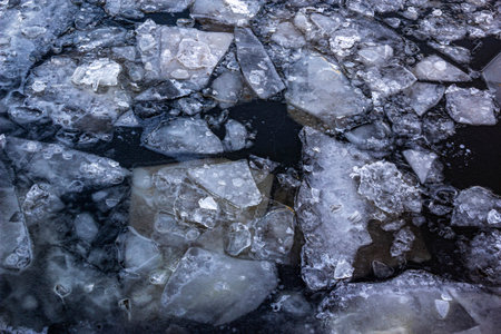 Broken ice of dark blue color on the river. Chunks of crushed ice on dark water. Abstract ice background. Blue background with cracks on the ice surface. Cracks of frozen waterの写真素材
