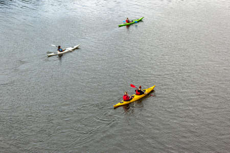 Four people on three kayaks are floating on a calm river. Several people are paddling a kayak....