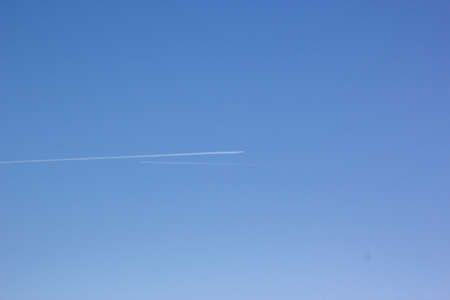 Two planes fly towards each other. Inversion trail of clouds from the plane against the blue sky. Airplane leaving vapor trail behind. Track in the sky from a jet plane.の写真素材