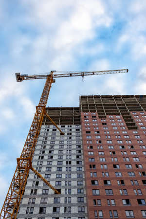 Construction crane is working on the construction of a multi-storey building, the view from the bottom of the crane on the construction crane and the building under construction against the skyの写真素材