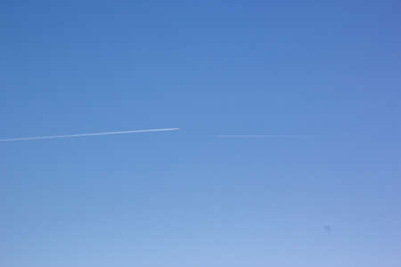 Two planes fly towards each other. Inversion trail of clouds from the plane against the blue sky. Airplane leaving vapor trail behind. Track in the sky from a jet plane.の写真素材
