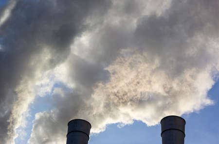 Air pollution by smoke coming out of two factory chimneys. Close-up from below of smoke coming out of pipes against blue sky. Concept air pollution, environmental problems, air emissionsの写真素材