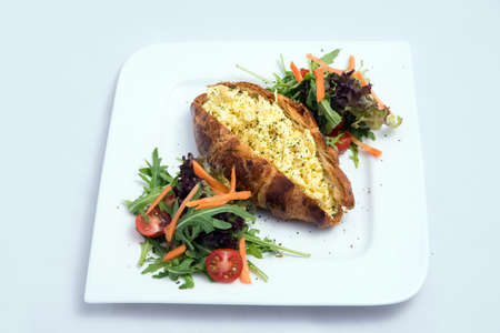 A low contrast image of a breakfast platter with egg-filled croissant with vegetables- carrot, tomato, lettuce on a minimal white background with a 30 degree angle from front perspectiveの写真素材