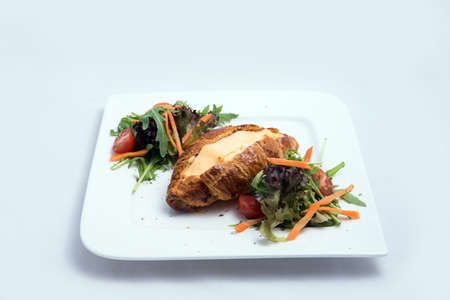 A low contrast image of a breakfast platter with cheese-filled croissant with vegetables- carrot, tomato, lettuce on a minimal white background with a 30 degree angle from front zoomed in perspectiveの写真素材
