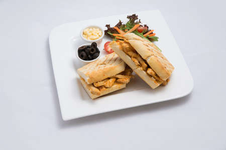 A low contrast Hero shot of a breakfast platter with grilled chicken panini sandwich with olives, cheese & vegetables- carrot, tomato, lettuce on a minimal white background with a 45 degree angle from almost front perspectiveの写真素材