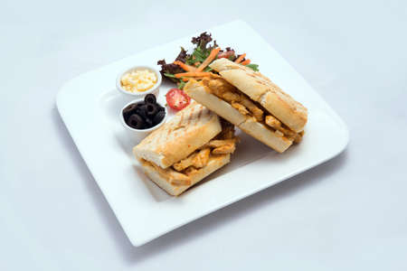A low contrast Hero shot of a breakfast platter with grilled chicken panini sandwich with olives, cheese & vegetables- carrot, tomato, lettuce on a minimal white background with a 45 degree angle from almost front perspectiveの写真素材
