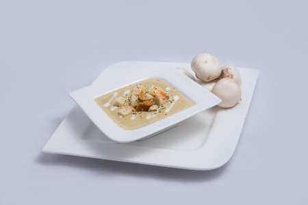 Contrasted Hero Shot of a Mushroom Soup with bread crumbs, oregano on a minimal white background with a 60 degree front facing angleの写真素材