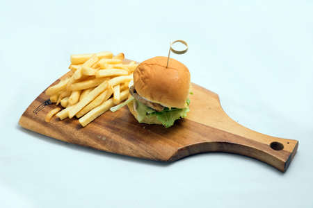 A low contrast Hero Shot of a grilled chicken slider burger, fries on a wooden platter board, on a minimal white background with a 45 degree angle from a diagonal perspectiveの写真素材
