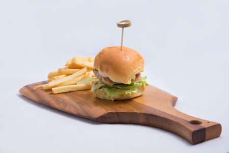 A low contrast Hero Shot of a grilled chicken slider burger, fries on a wooden platter board, on a minimal white background with a 45 degree angle from a diagonal perspectiveの写真素材