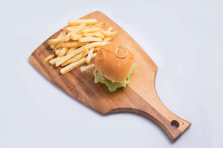 A low contrast Hero Shot of a grilled chicken slider burger, fries on a wooden platter board, on a minimal white background with a 45 degree angle from a diagonal perspectiveの写真素材
