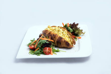 A low contrast image of a breakfast platter with egg-filled croissant with vegetables- carrot, tomato, lettuce on a minimal white background with a 30 degree angle from front perspectiveの写真素材