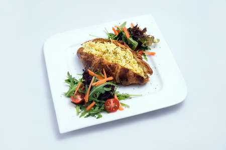 A low contrast image of a breakfast platter with egg-filled croissant with vegetables- carrot, tomato, lettuce on a minimal white background with a 30 degree angle from front perspectiveの写真素材