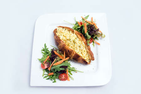 A low contrast image of a breakfast platter with egg-filled croissant with vegetables- carrot, tomato, lettuce on a minimal white background with a 30 degree angle from front perspectiveの写真素材
