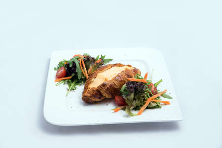 A low contrast image of a breakfast platter with cheese-filled croissant with vegetables- carrot, tomato, lettuce on a minimal white background with a 30 degree angle from front zoomed in perspectiveの写真素材