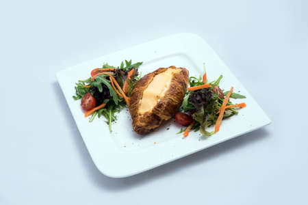 A low contrast image of a breakfast platter with cheese-filled croissant with vegetables- carrot, tomato, lettuce on a minimal white background with a 30 degree angle from front zoomed in perspectiveの写真素材