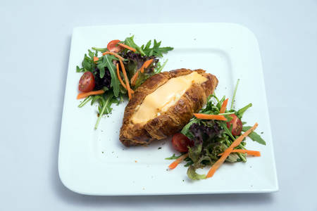 A low contrast image of a breakfast platter with cheese-filled croissant with vegetables- carrot, tomato, lettuce on a minimal white background with a 30 degree angle from front zoomed in perspectiveの写真素材