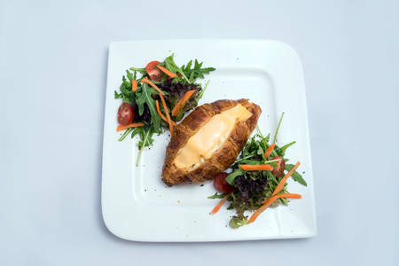 A low contrast image of a breakfast platter with cheese-filled croissant with vegetables- carrot, tomato, lettuce on a minimal white background with a 30 degree angle from front zoomed in perspectiveの写真素材
