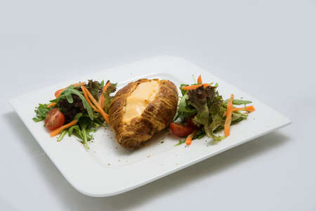A low contrast image of a breakfast platter with cheese-filled croissant with vegetables- carrot, tomato, lettuce on a minimal white background with a 30 degree angle from front zoomed in perspectiveの写真素材