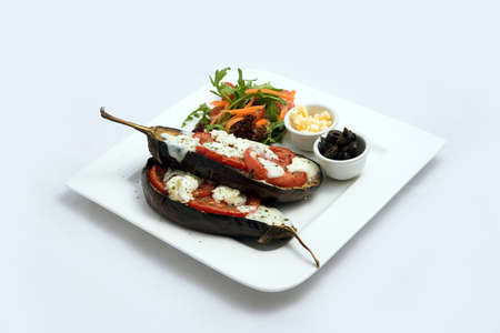 A low contrast warm Hero shot of a main course platter with grilled aubergine with buffalo cheese, tomato, olives & vegetables on the side, on a minimal white background with a 45 degree angle from diagonal perspective.の写真素材